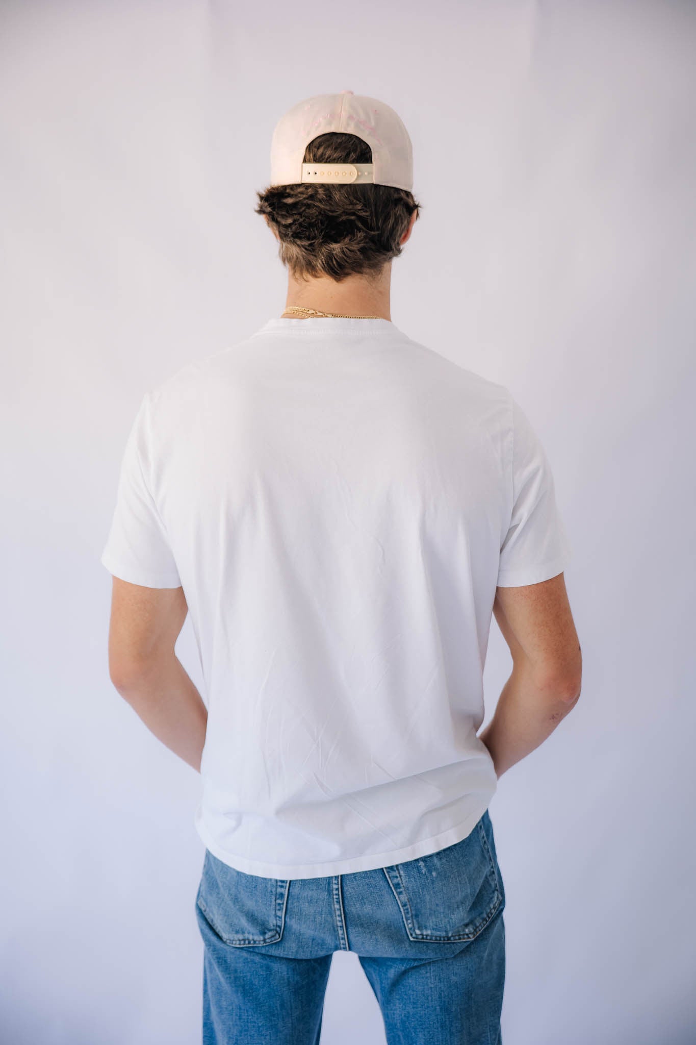 Person wearing a white t-shirt and blue jeans with a pink cap on a plain background