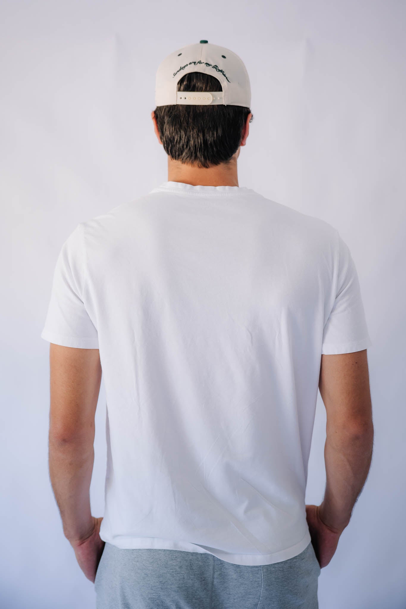 Person wearing a white t-shirt and green forest cap from behind on a plain background