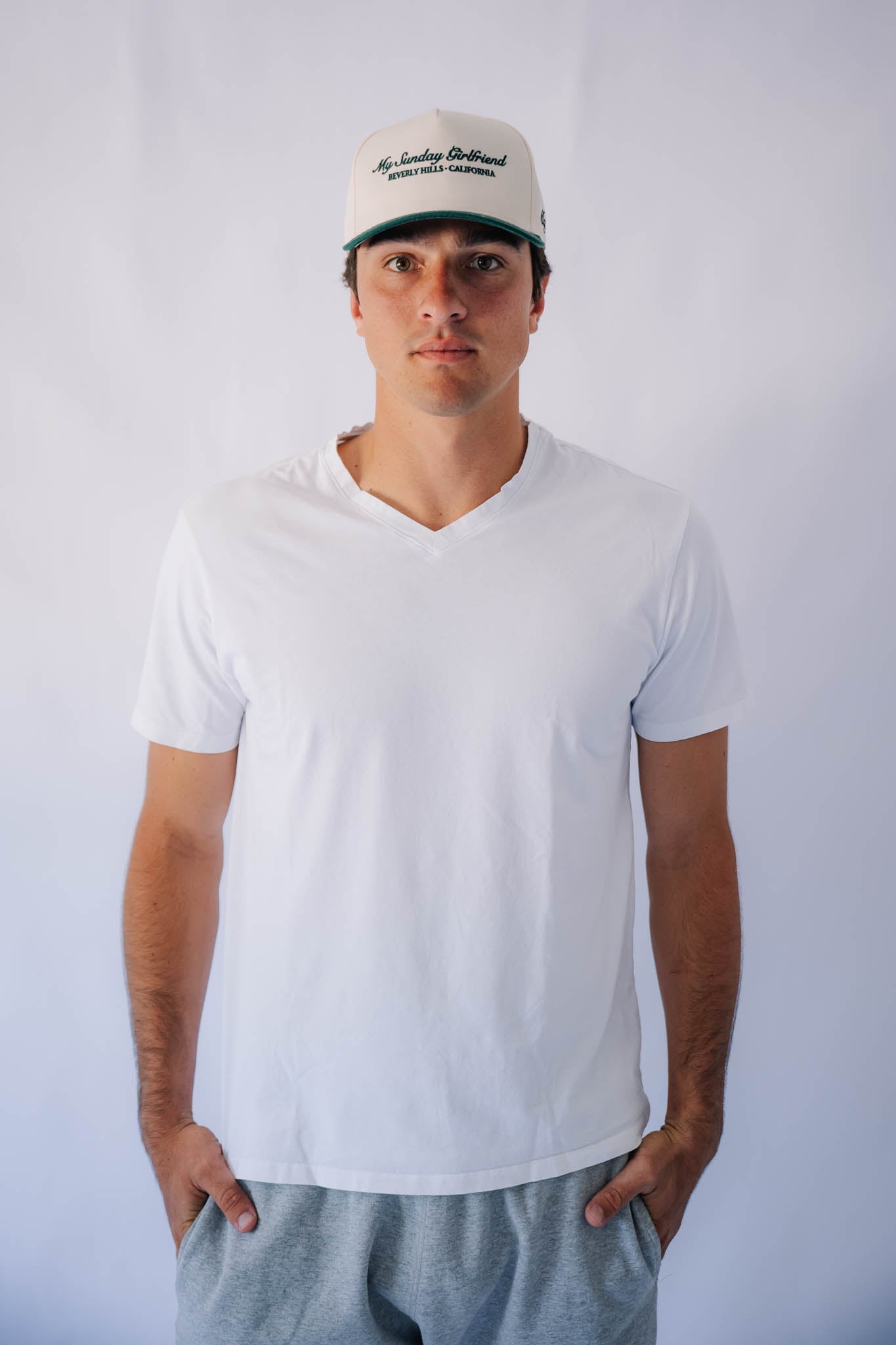 Man wearing a white t-shirt and green  forest cap against a plain background