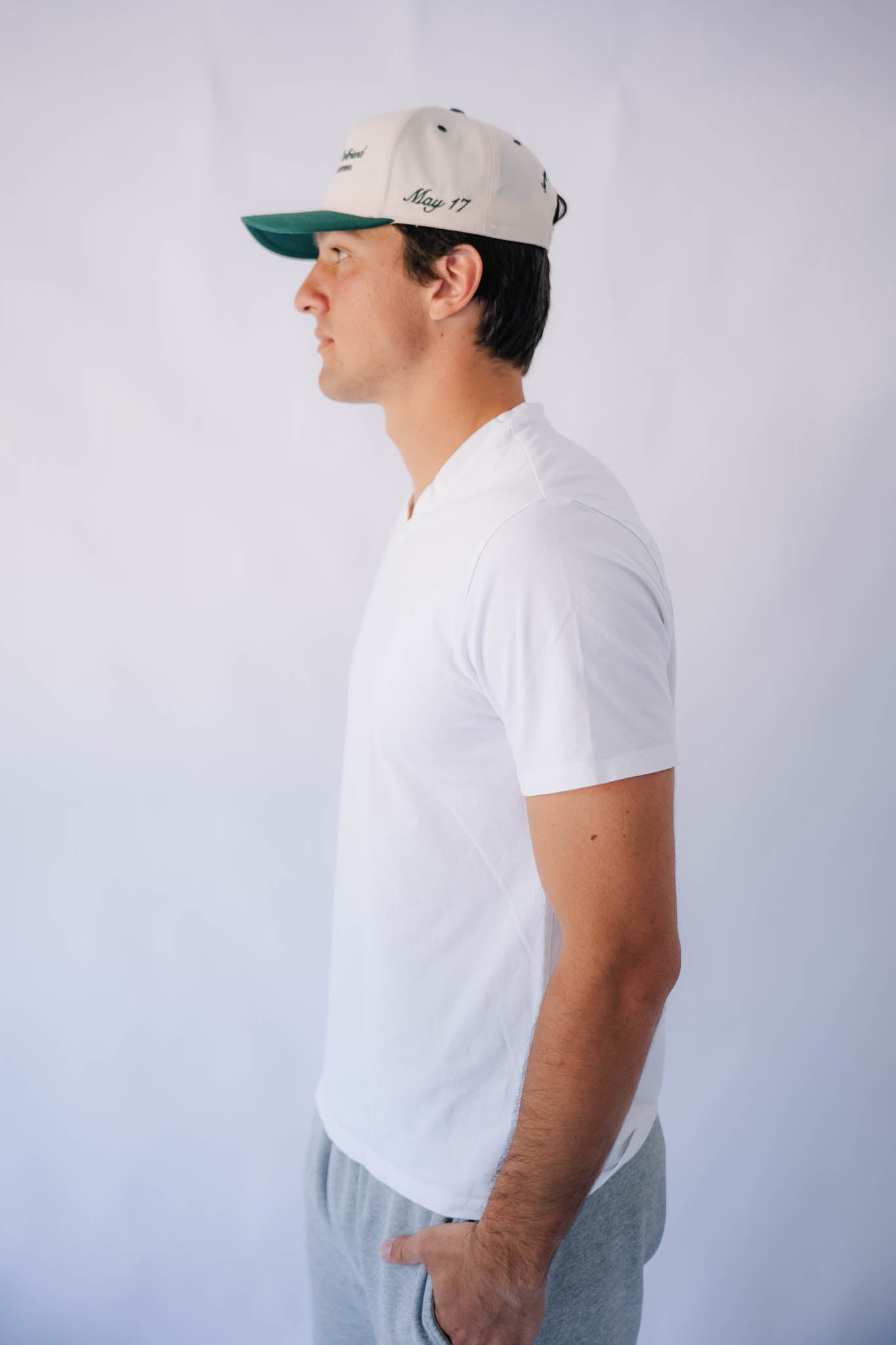 Man wearing a white t-shirt and green forest cap against a plain background