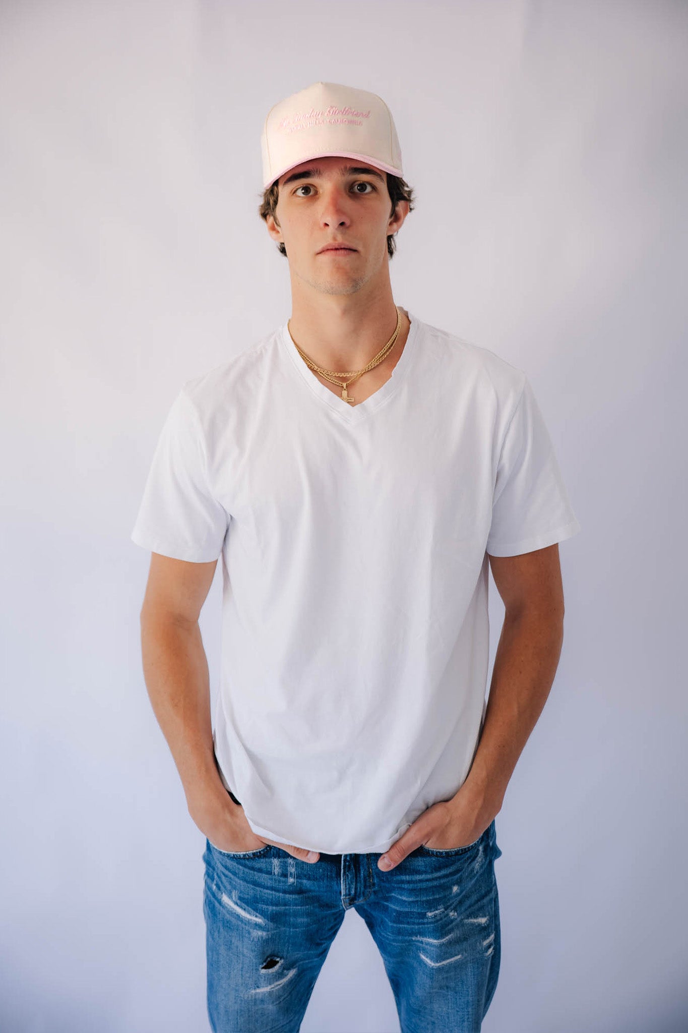 Person wearing a white t-shirt, blue jeans, and a pink cap against a plain background