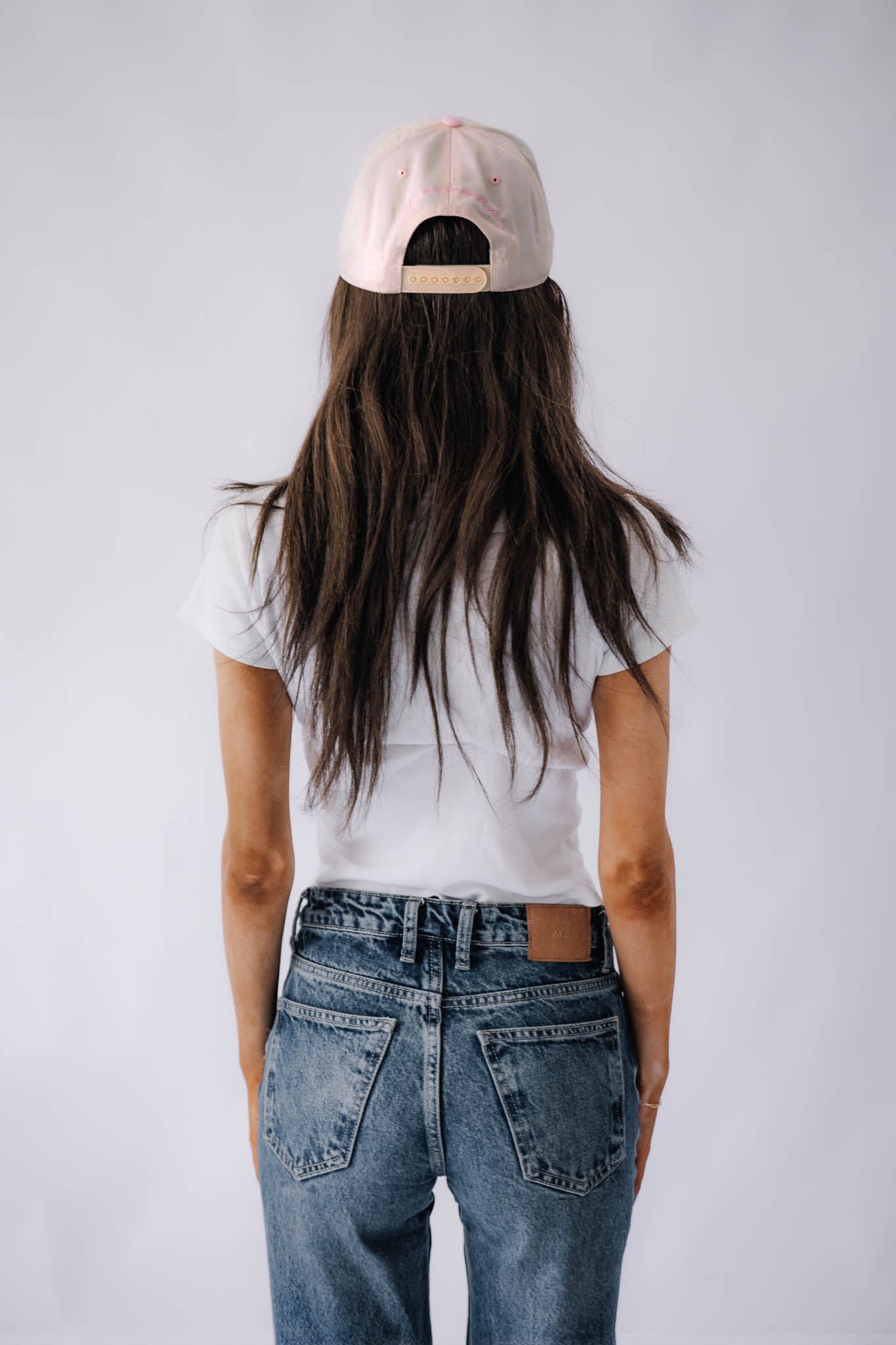 Person wearing a pink cap, white t-shirt, and blue jeans from behind on a plain background